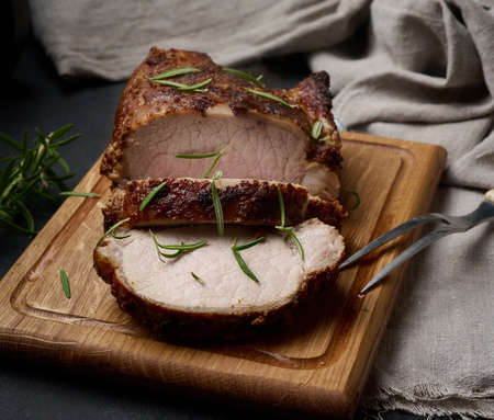 baked piece of pork meat in spices on a wooden board, cut into pieces. Eye of round roast steakの写真素材
