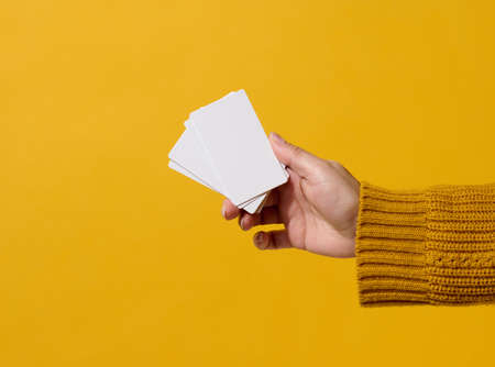 Female hand holding empty paper white business card on a yellow background. Copy spaceの写真素材