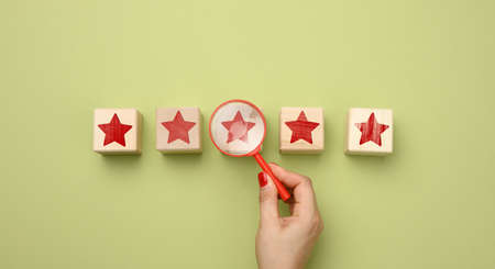 five red stars and a hand with a plastic magnifier on a green background. Evaluation of the quality...