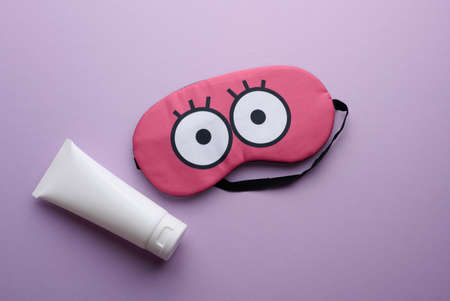 white plastic tube for cosmetics and pink textile sleep mask on purple backgroundの写真素材