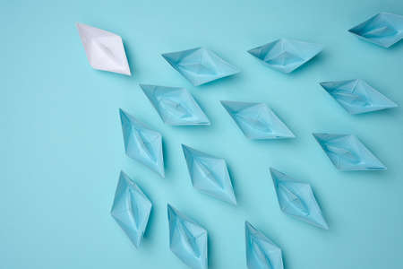 a group of blue paper boats follow white against a light blue background. Strong leader concept,...