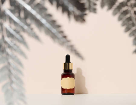 brown glass bottle with a pipette stands on a brown background. Container for cosmetics, serum and oil, silver fern leafの写真素材