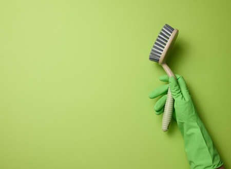hand in a green rubber glove holds a plastic cleaning brush on a green backgroundの写真素材