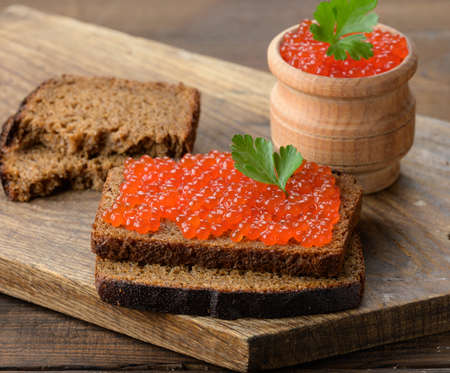 red salmon caviar lies on a piece of rye bread. Brown wooden tableの写真素材