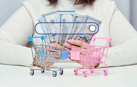 a woman is holding American paper dollars in her hands and two miniature shopping carts on the...