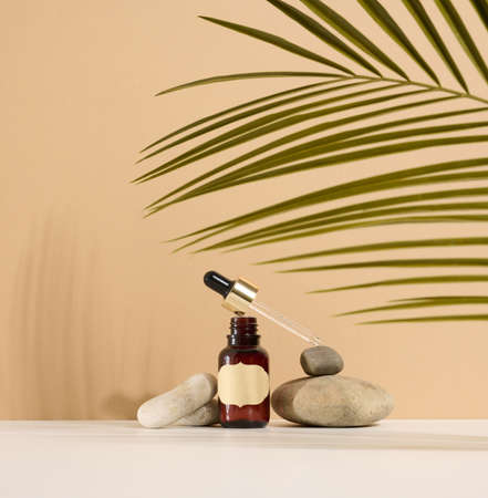 a brown glass bottle with a pipette and a brown label stands on a stone. Container for cosmetics, serum and oil. Palm leaf shadowの写真素材