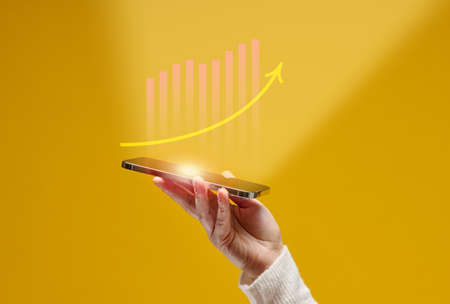 female hand holds a smartphone with holographic graphics on a yellow background. Performance growth, successの写真素材