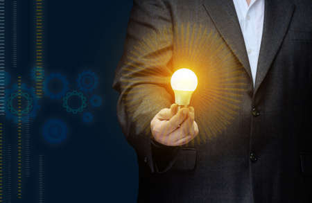 A businessman holds an electric lamp in his hand on a dark blue background. Concept of new ideas in...