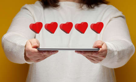 woman holds an electronic tablet and five red hearts over it. Feedback concept, business ratingの写真素材