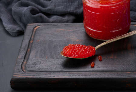 fresh grainy red caviar in a glass jar on a wooden tableの写真素材