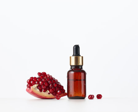 brown glass bottle with a pipette and red pomegranate seeds on a white background. Template for cosmetic liquid products, advertising and promotionの写真素材