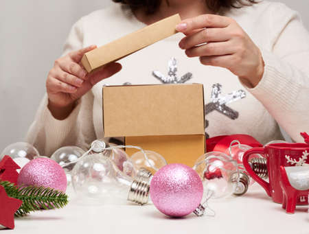 woman in a white sweater sits at the table and wraps gifts for Christmas. Preparing for the holidays
