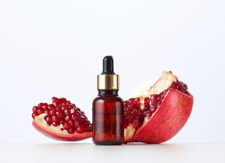 brown glass bottle with a pipette and red pomegranate seeds on a white background. Template for cosmetic liquid products, advertising and promotionの写真素材