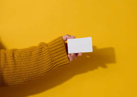 Female hand holding empty paper white business card on a yellow background. Copy spaceの写真素材