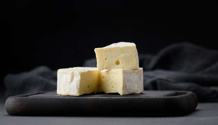 round brie cheese on brown wooden cutting board, black background
