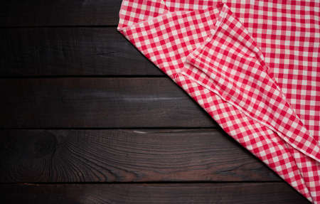 folded red and white cotton kitchen napkin on a wooden brown background, top view, copy space