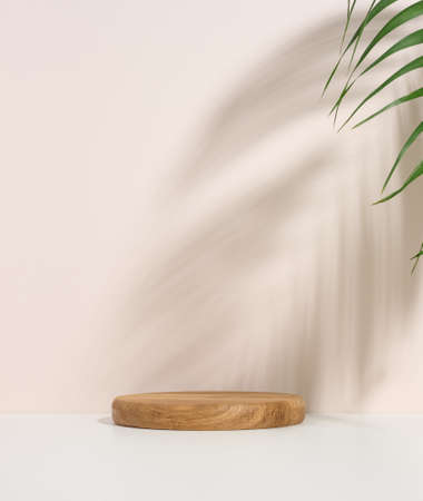 stage for displaying products, cosmetics with a round wooden podium and a green palm leaf. Shadow on the backgroundの写真素材