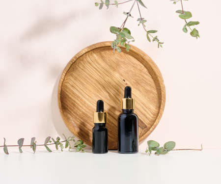 glass brown bottle with a pipette on a wooden podium and a branch of eucalyptus. Advertising and promotion of cosmetic productsの写真素材
