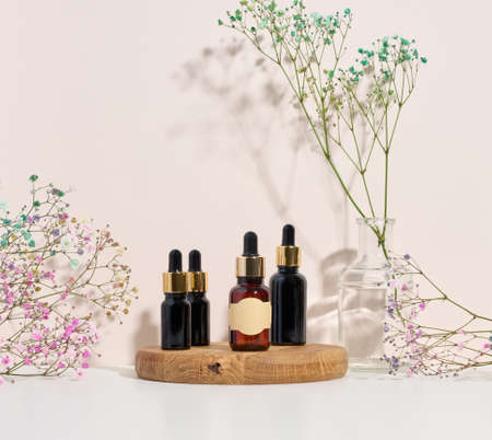 glass brown bottle with a pipette on a wooden podium and a branch of flowers. Advertising and promotion of cosmetic productsの写真素材