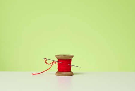 wooden spool with red wool thread and a large needle on a white table. Handicraft itemsの写真素材