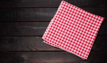 folded red and white cotton kitchen napkin on a wooden brown background, top view, copy space