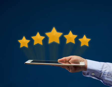 a female hand holds an electronic tablet and five yellow virtual stars above the screen. User rating...