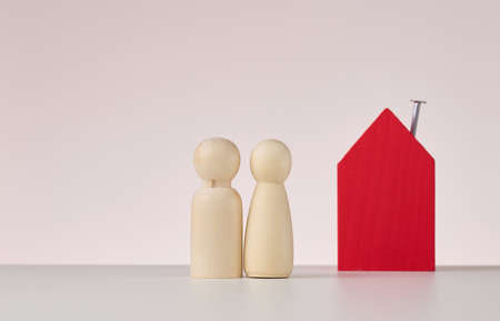 wooden figures of men and a miniature house on a beige background. The concept of buying or selling...