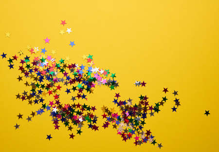 shiny multicolored star confetti scattered on a yellow background, festive backdrop for birthday, valentines day. Festive decoration element. Flat design, copy spaceの写真素材