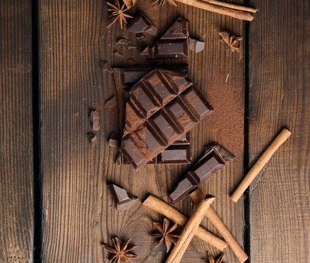 broken pieces of dark chocolate, cinnamon sticks and star anise on a brown wooden table, top viewの写真素材