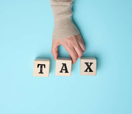 female hand holds a wooden cube with the inscription tax on a blue background.の写真素材