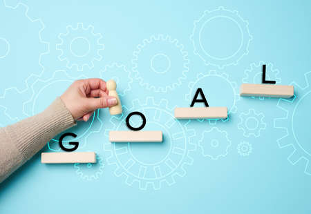 a female hand holds a wooden figurine on a blue background and wooden blocks. The concept of achieving the goal, the way forwardの写真素材