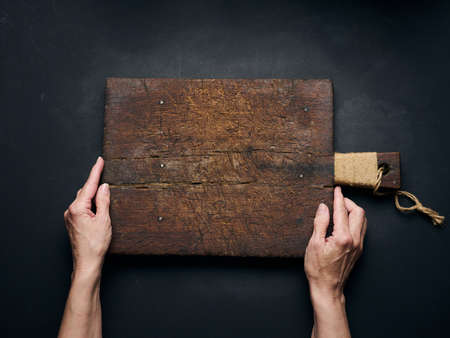 Empty wooden cutting board in female hands on black wooden table, top viewの写真素材