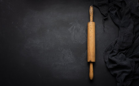 Old wooden rolling pin for rolling dough on a black background, top view. copy space