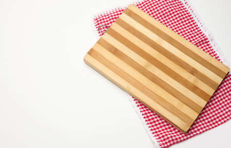 empty rectangular wooden kitchen cutting board and red towel in a white cage on a white table, top...