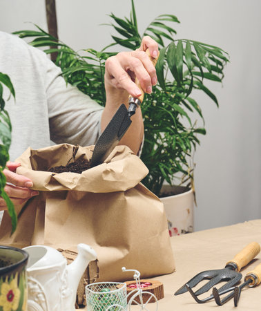 A woman in gray clothes holds a bag of soil for planting seeds in paper cups. Hobby and leisureの写真素材