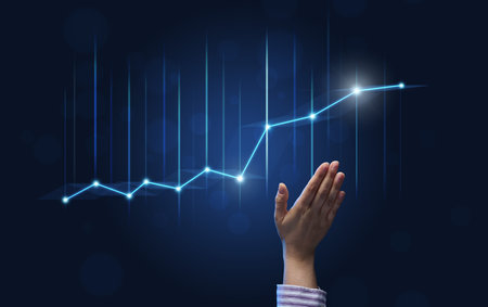 a businessman's hand points to a holographic graph with rising rates on a blue background. Development of a business with high profits, the prospect of implementing business plansの写真素材