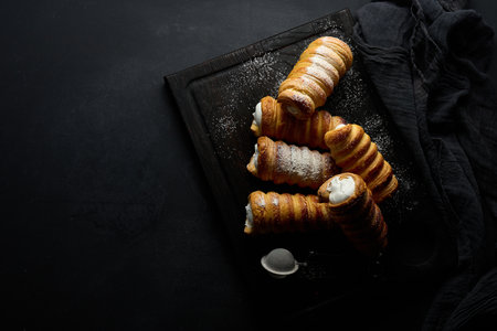 baked tubules filled with whipped egg white cream on a black wooden kitchen board, top viewの写真素材