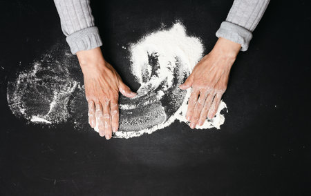 Sifted white wheat flour on a black table and two female hands, top view. cooking at homeの写真素材