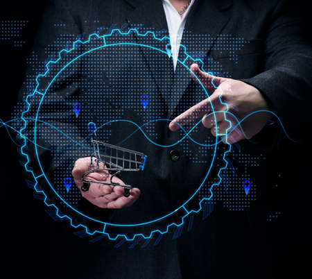 Man in a black suit holds a miniature cart against the background of a holographic graph with increasing indicators. Growth in business sales, high margins. big profitの写真素材