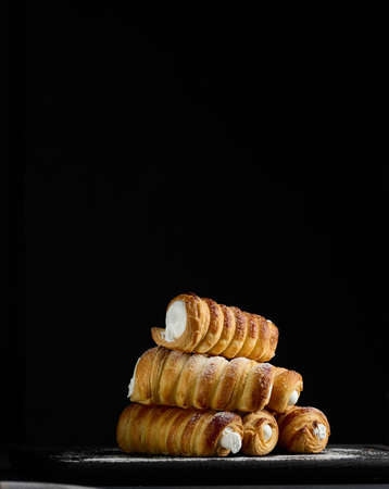 Baked tubules filled with whipped egg whites cream on a black wooden kitchen board