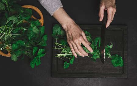 Woman cutting green mint leaves on brown wooden cutting board, top viewの写真素材