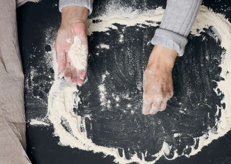 Sifted white wheat flour on a black table and two female hands, top view. cooking at homeの写真素材