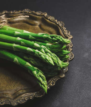 fresh green asparagus sprouts on a round copper plate, black background. View from aboveの写真素材