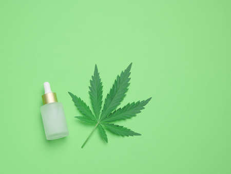 White glass bottle with pipette and green cannabis leaf on a green background, top viewの写真素材
