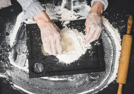 two female hands knead the dough from white wheat flour on a black table, top viewの写真素材