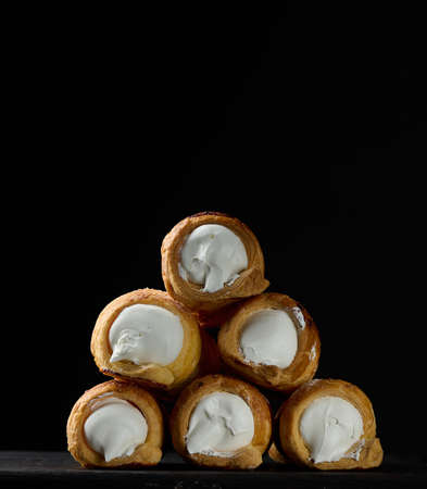 Baked tubules filled with whipped egg whites cream on a black wooden kitchen board