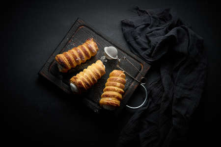baked tubules filled with whipped egg white cream on a black wooden kitchen board, top view