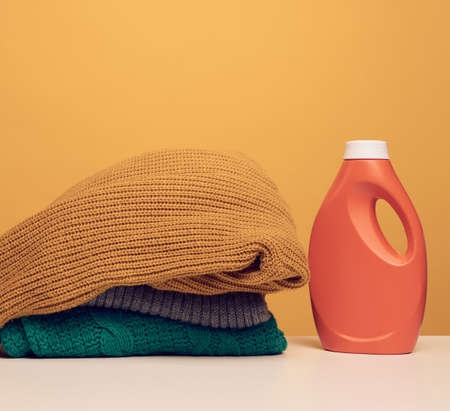 stack of washed folded clothes and plastic orange large bottle with liquid detergent stand on a...