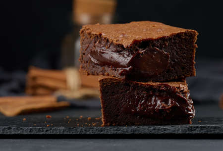 Baked pieces of chocolate brownie pie on black table, delicious dessert