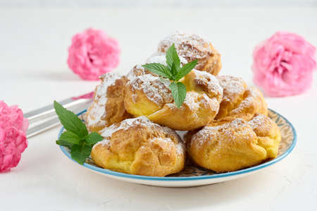 Baked eclairs with custard cream on a metal round plate sprinkled with powdered sugar
